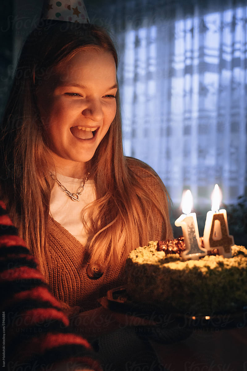 Teenager girl celebrating 14 Birthday, blowing out candles on cake