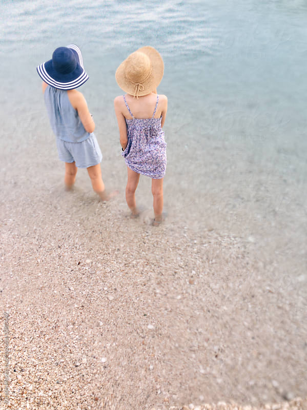 Two teenage girls, wearing hats and standing with their feet in the sea.