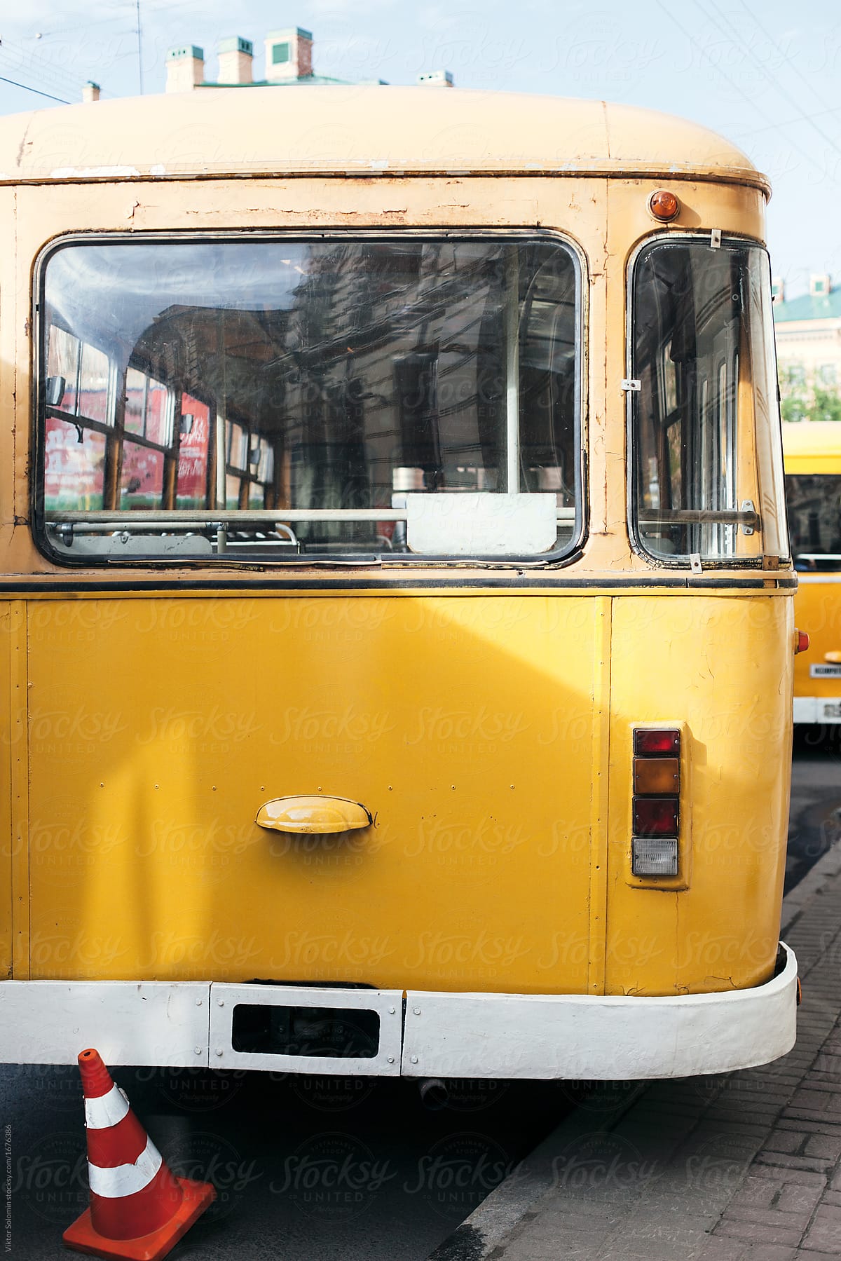 Back view of yellow vintage city bus standing on the parking near red road cone