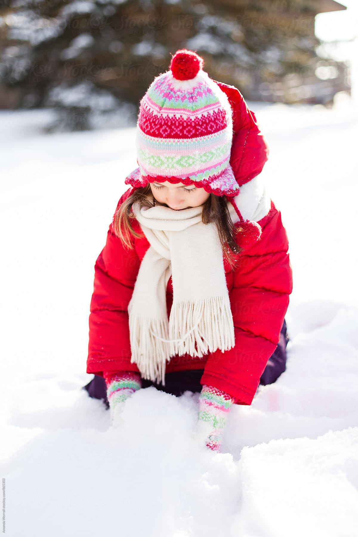 Young girl wearing colorful snow gear scoops up snow in her mittens