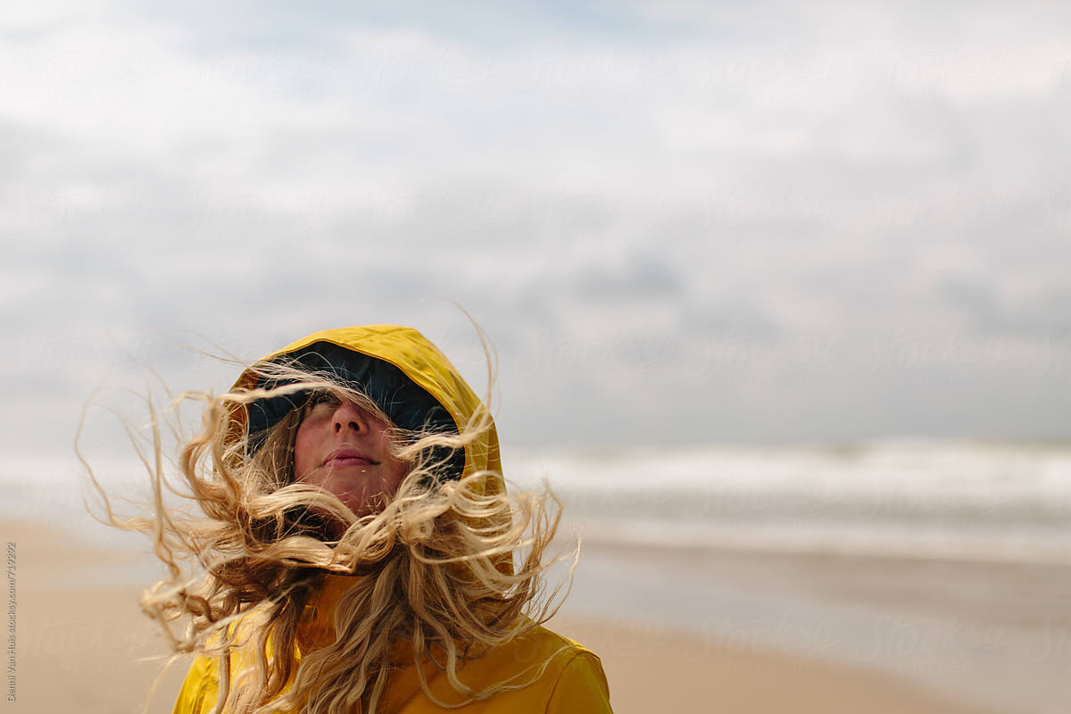 A Blond Woman On A Windy Beach With Her Hair Blowing Everywhere By