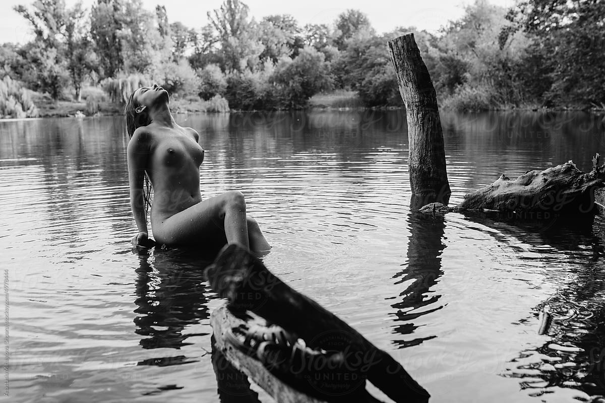 Portrait of nude tanned woman sitting on the bank of the river water