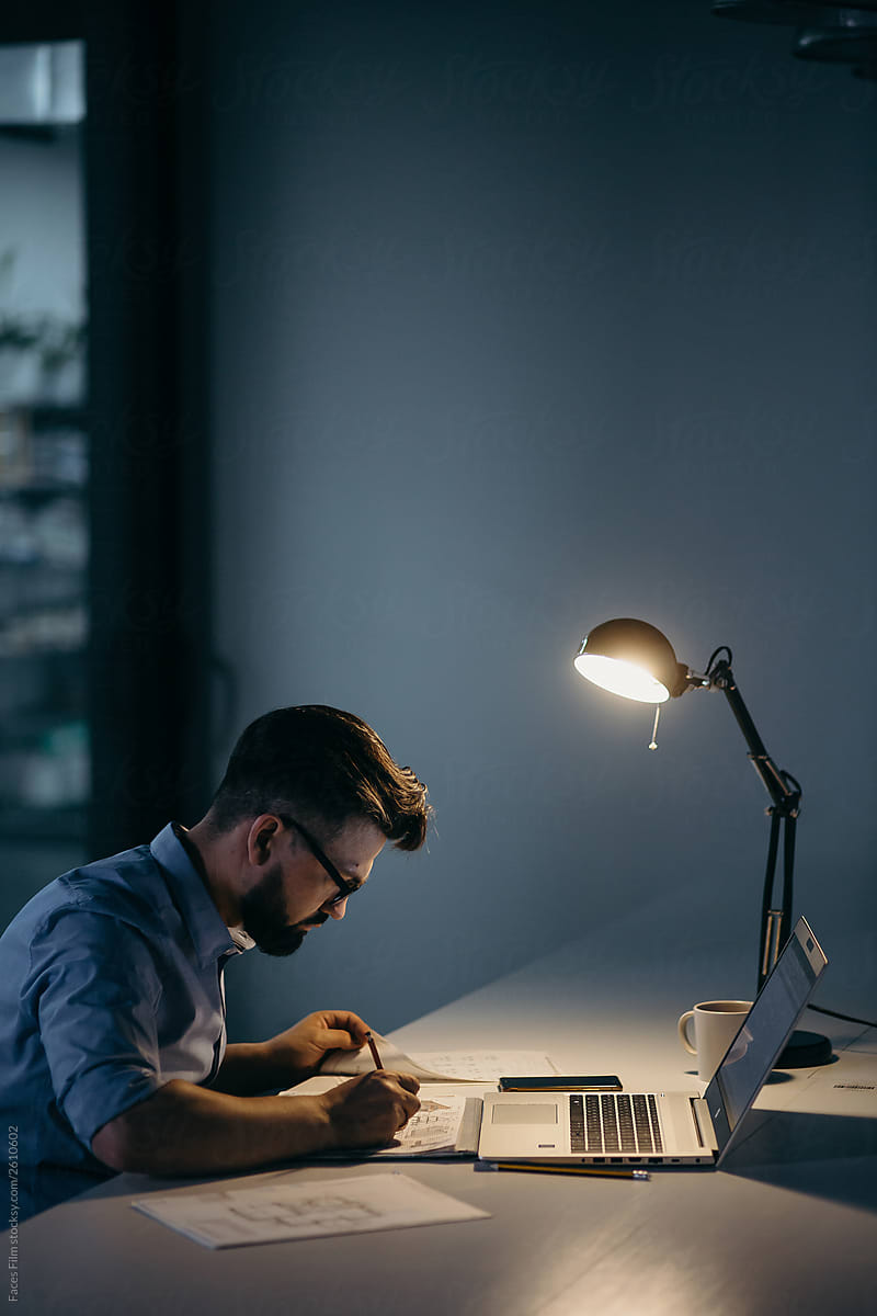 Modern man with glasses and beard working at night in his office alone
