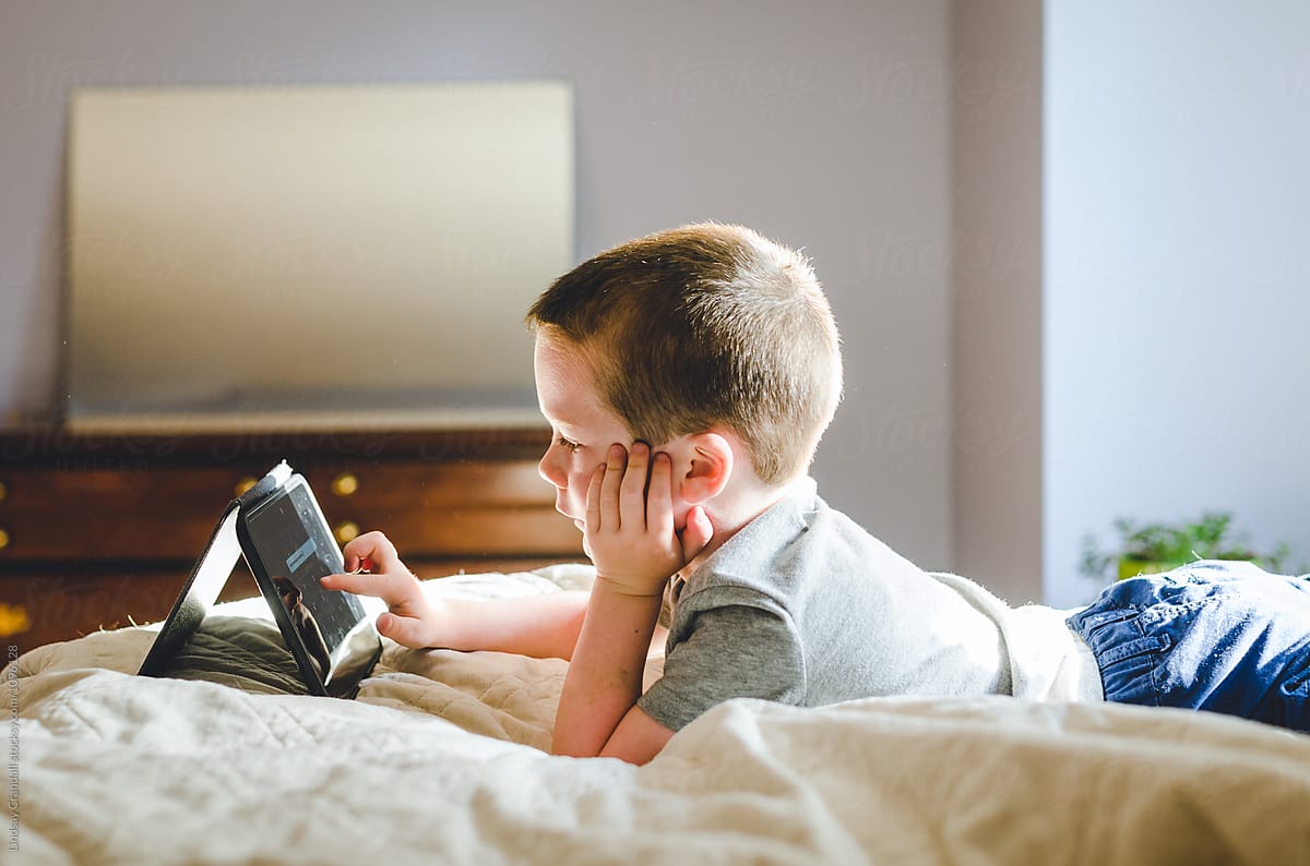 Young boy lying on bed playing with a tablet