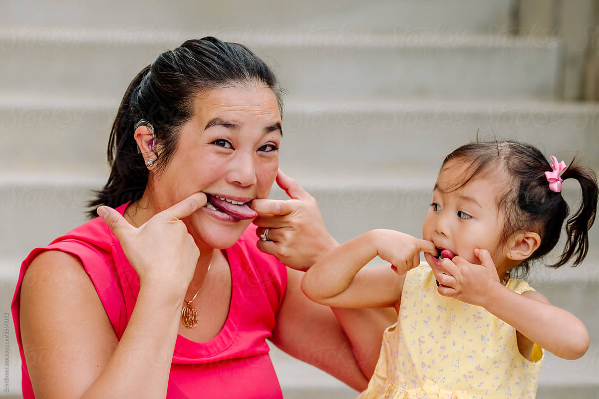 Young girl imitates Asian mom with cochlear implant making silly faces
