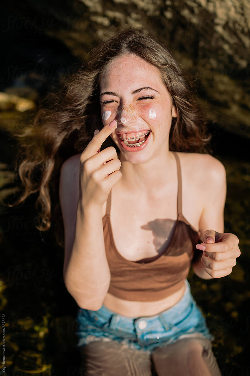 Happy summer portrait of a teenage laughing girl putting on sunscreen