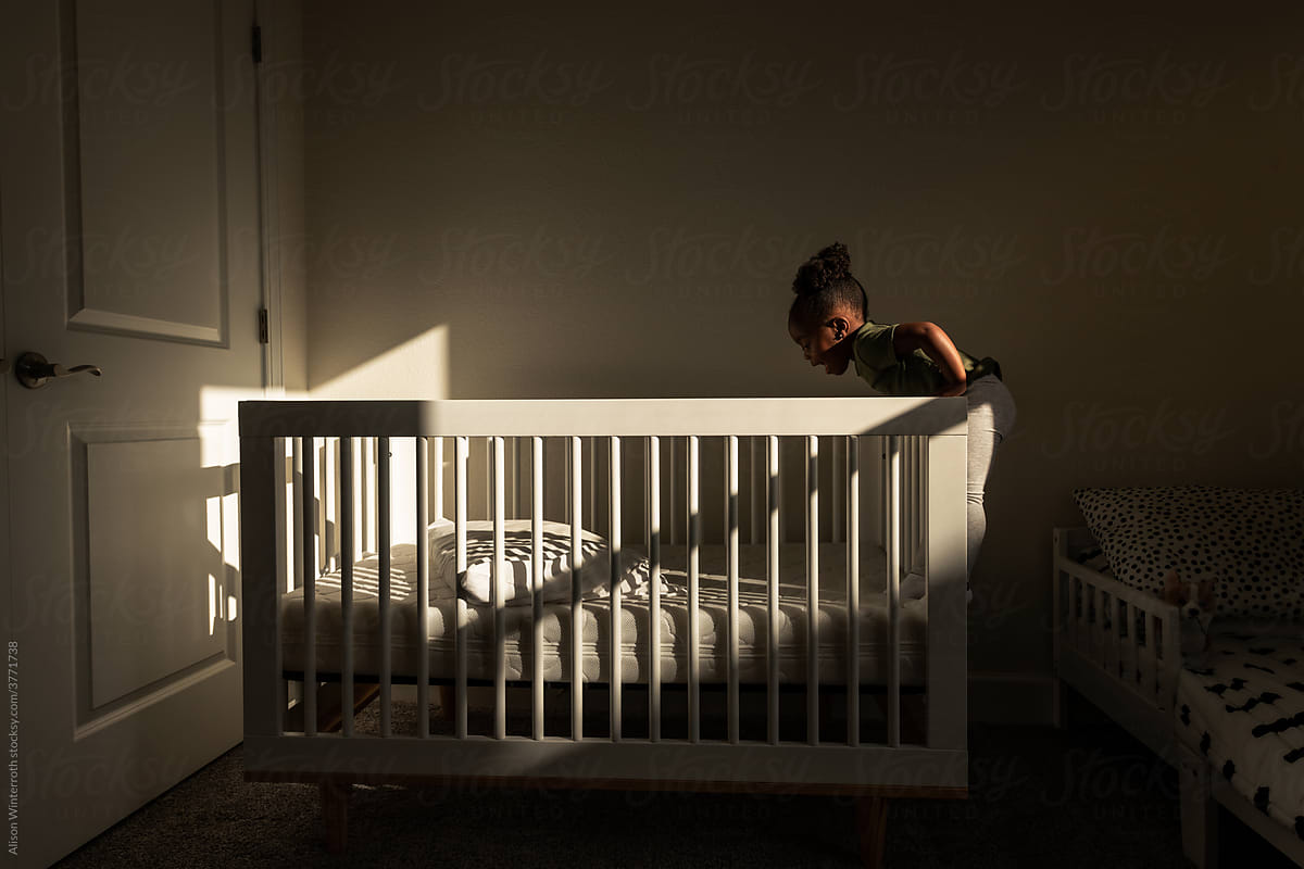 Toddler leans over the edge of her crib