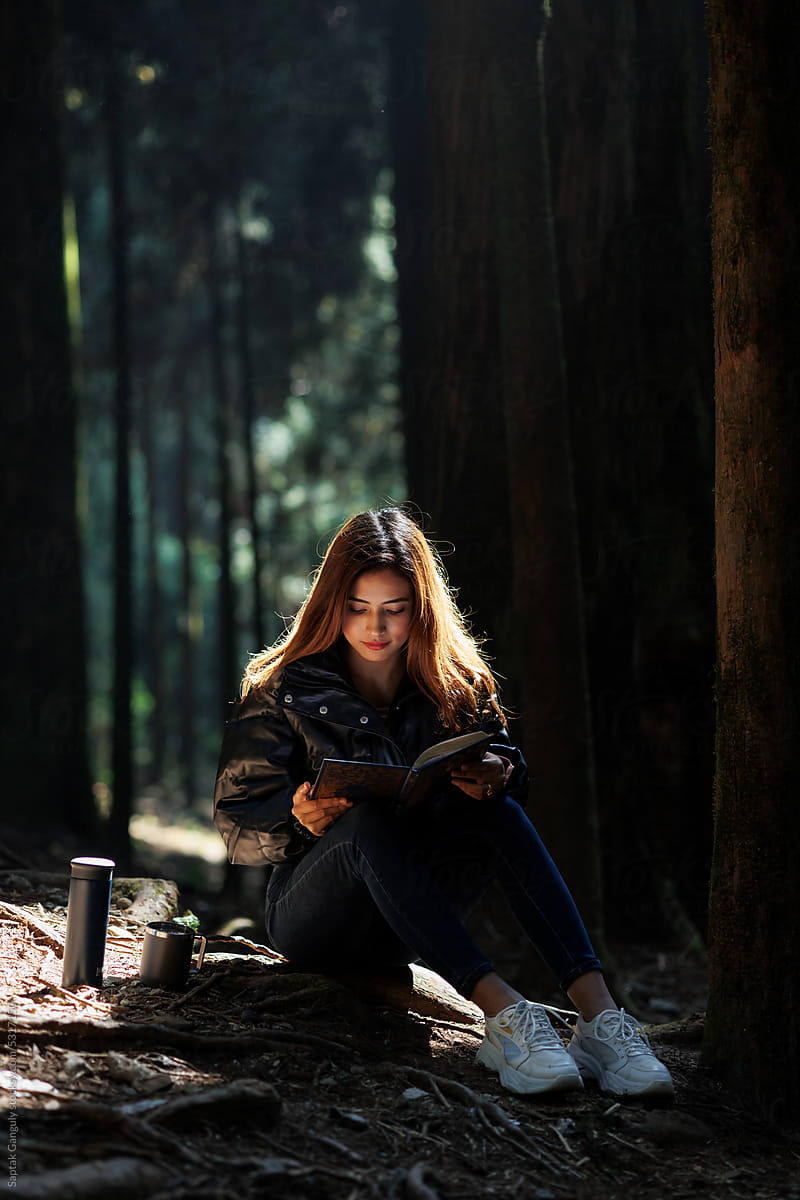 Young woman relaxing and reading a book in the woods