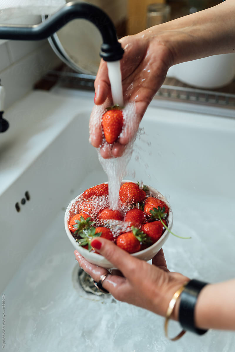 Woman washing strawberries under a running water