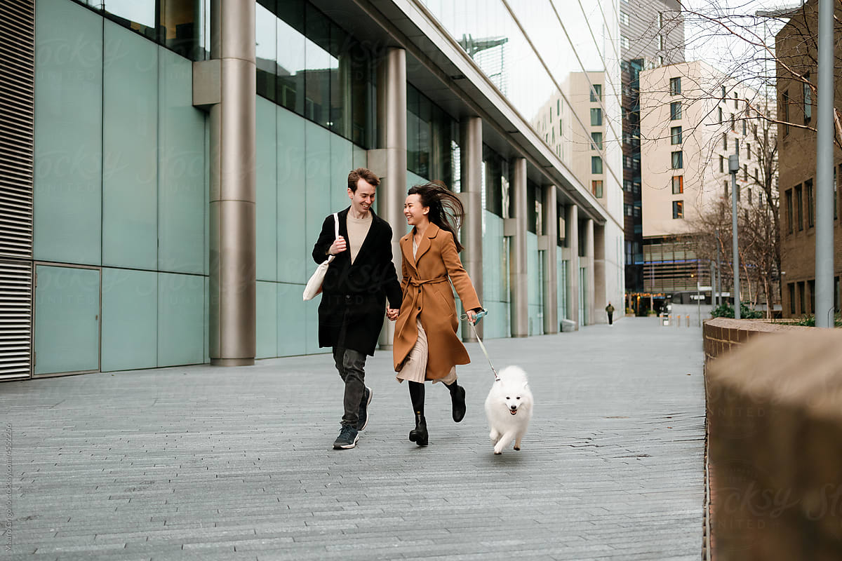 A couple runs and has fun with their dog in the city