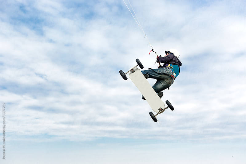 Young man jumping high in the air with his kite while riding an All-Terrain Board
