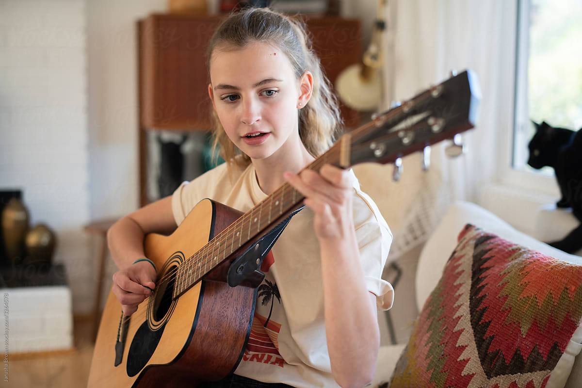 Teenage girl plays acoustic guitar in living room.