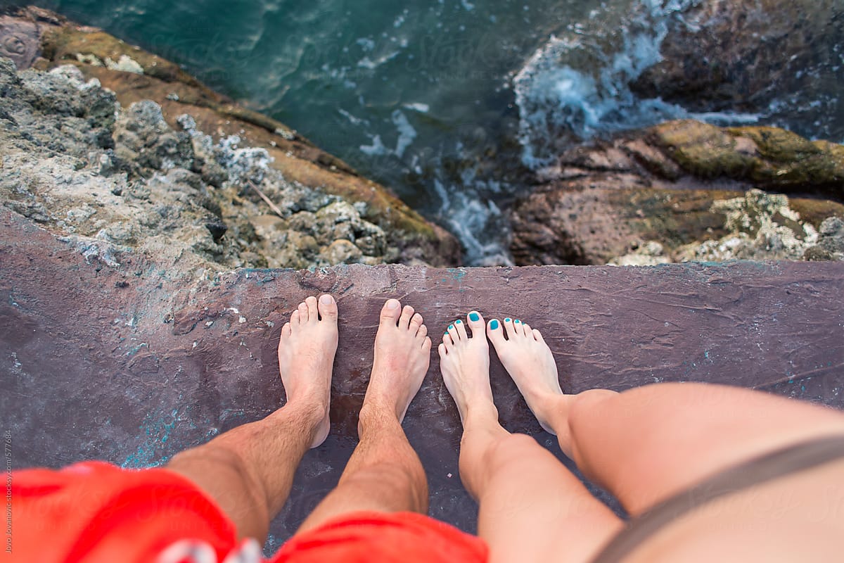 Feet of a couple looking at the ocean from above