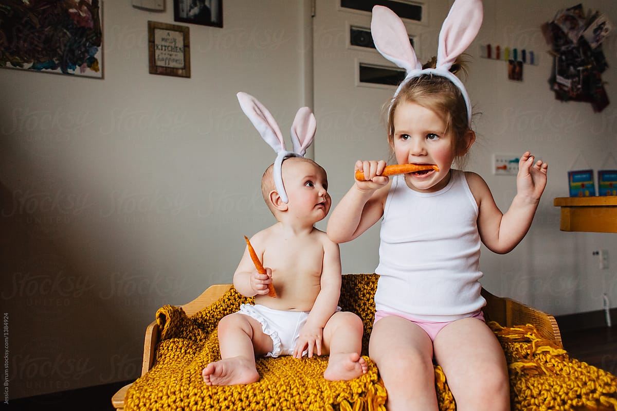Toddler and baby sisters dressed up and eating carrots for Easter.