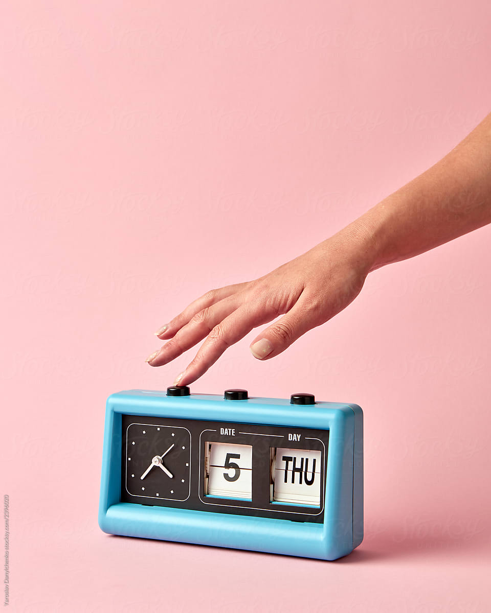 Woman's hand turns off the button on retro flip clock with calendar day thuesday, date 5, on a background color of the year 2019 Living Coral .