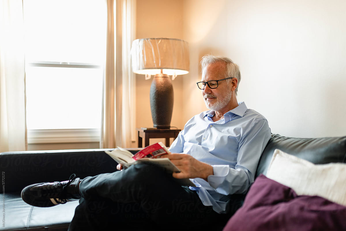 Older Man Enjoys Reading a Book While Sitting on His Living Room Couch