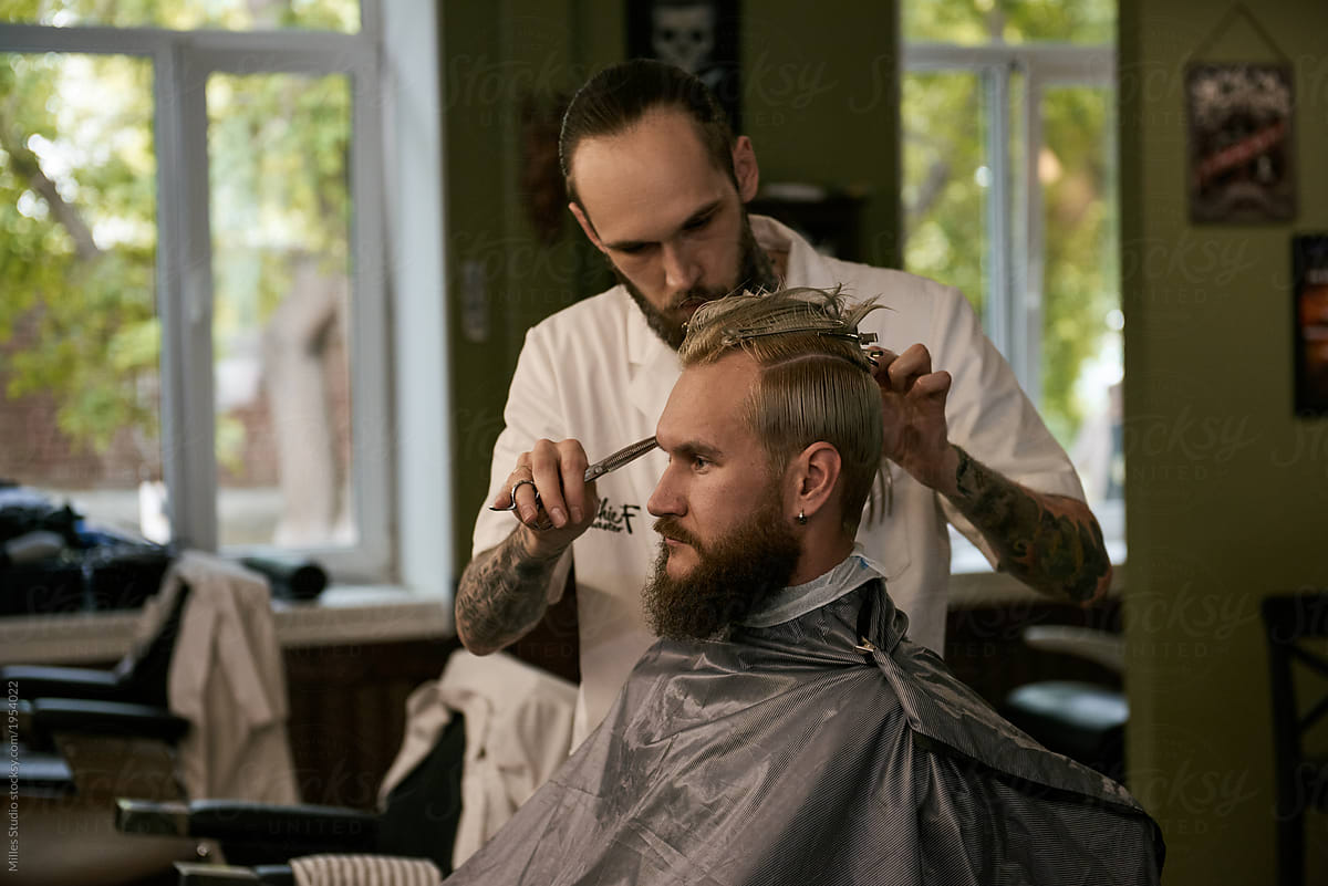 Serious barber cutting handsome client in chair