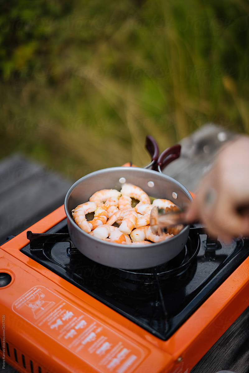 Person cooking shrimps in pan on camping stove