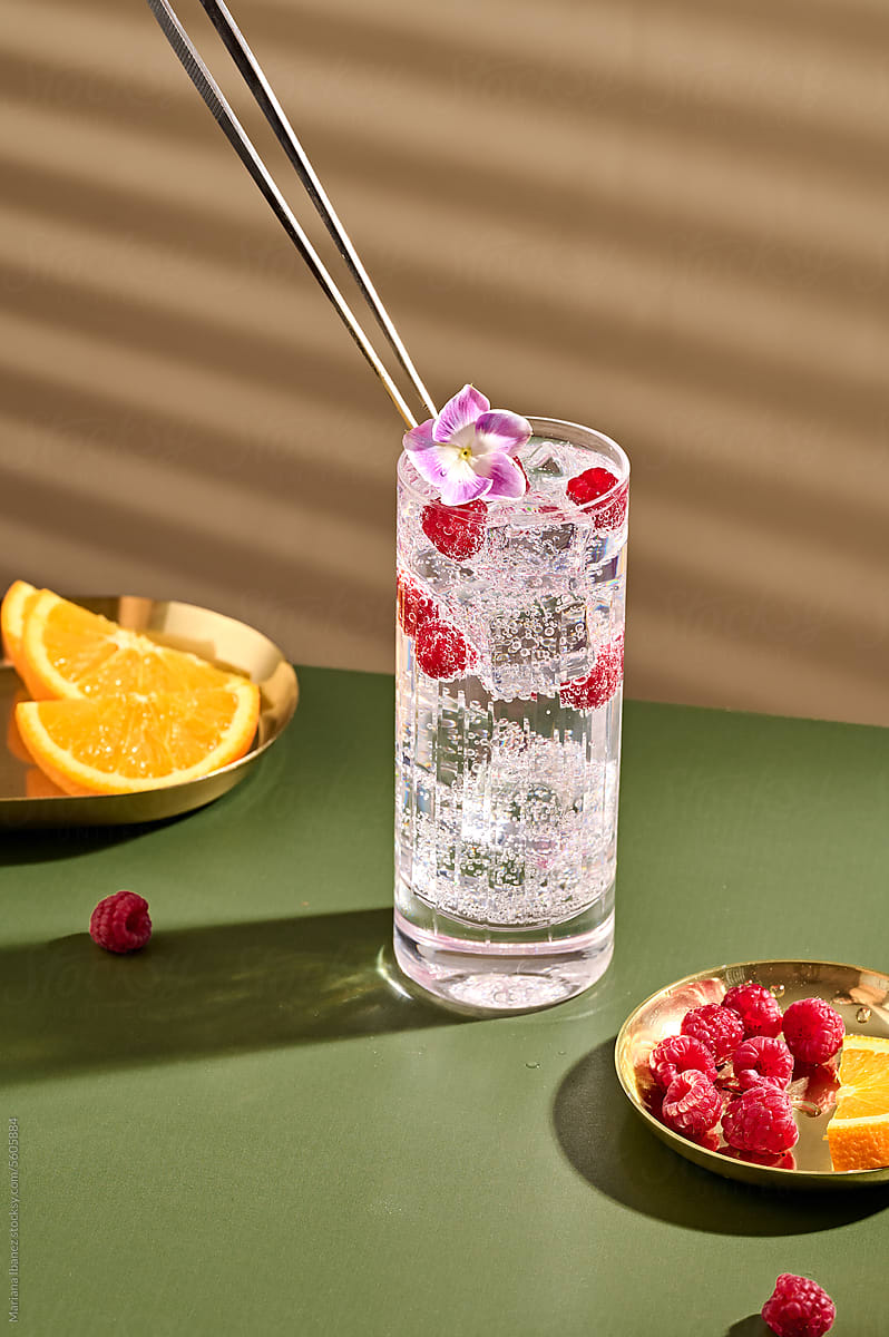glass of Vodka soda with rasperries and flower garnish.
