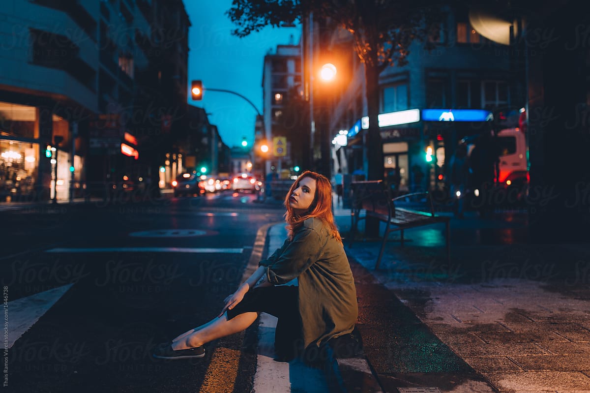 woman sitting on the border of the road at dusk