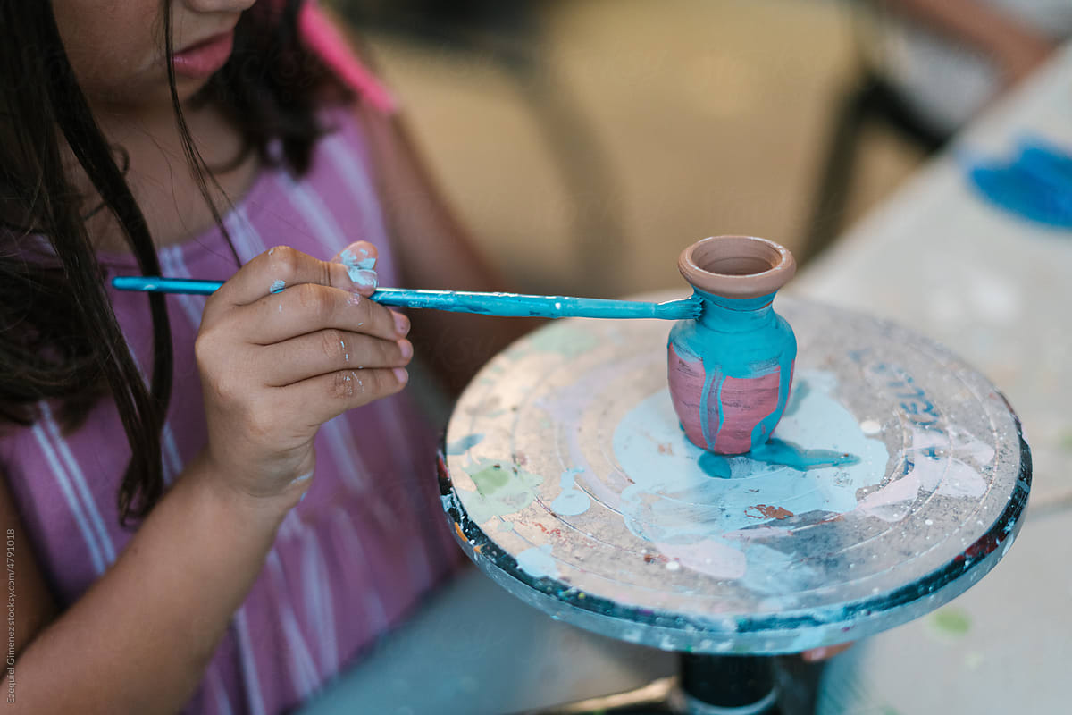 Anonymous girl painting clay vase in workshop