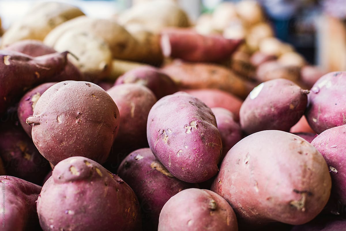 Close up of red potatoes and orange yams resting in a pile at a market.