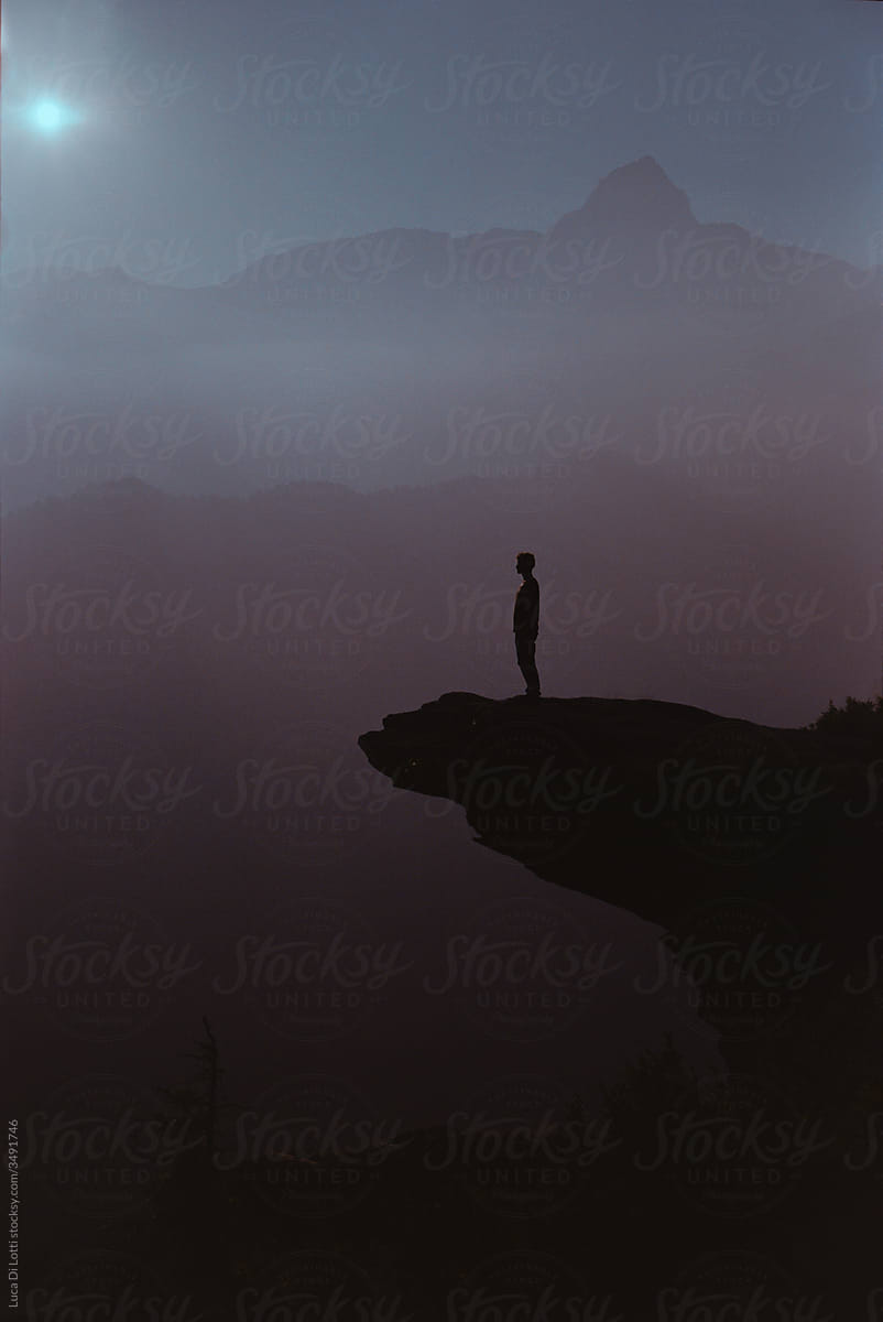 Silohuette of a Man standing on a protruding rock on Alps at sunset