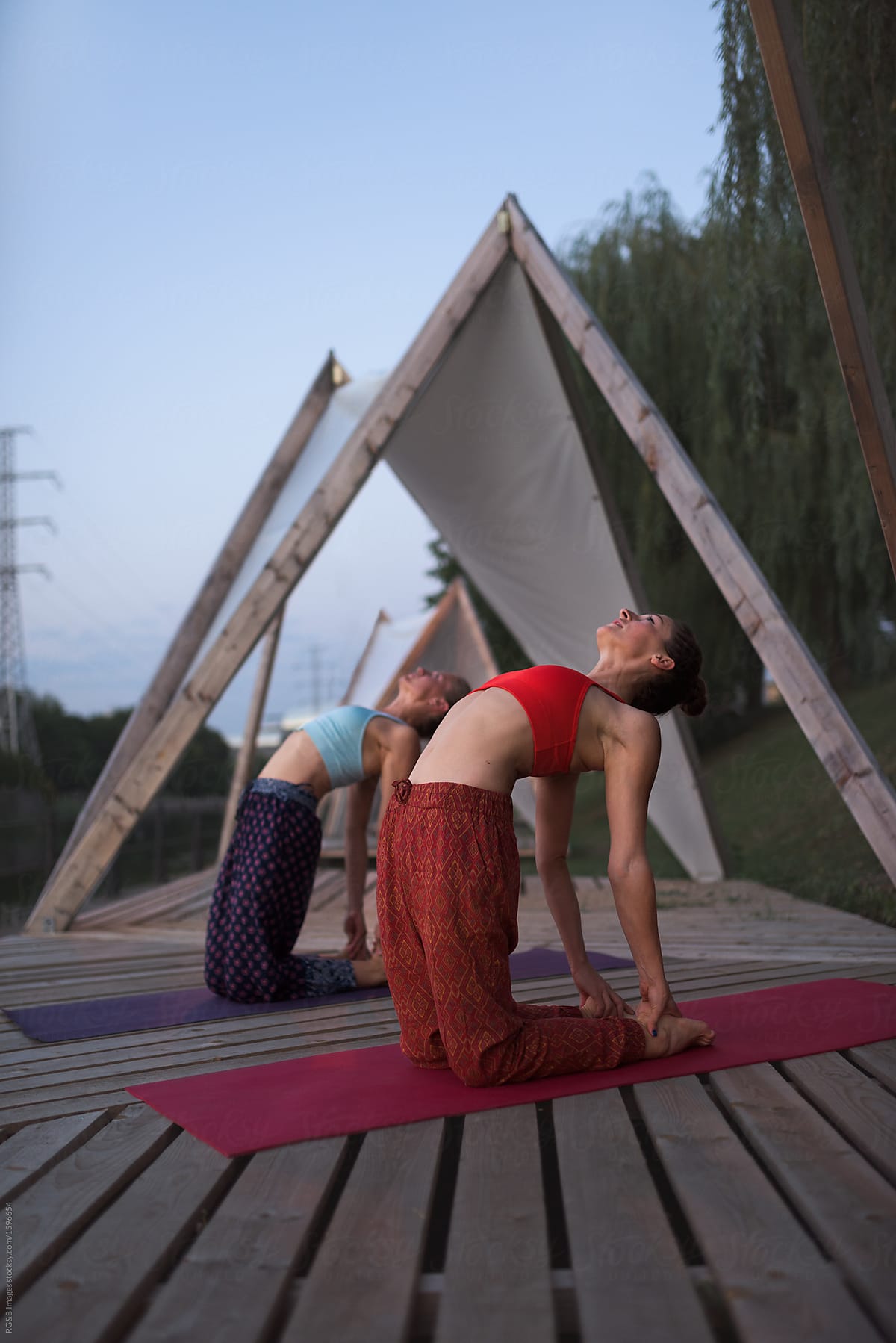 Two women practicing yoga outdoor on wooden pontoon