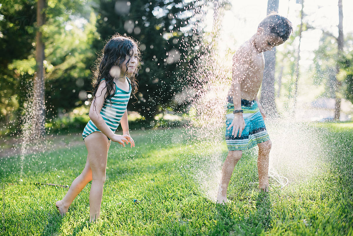 Young siblings playing in a sprinkler