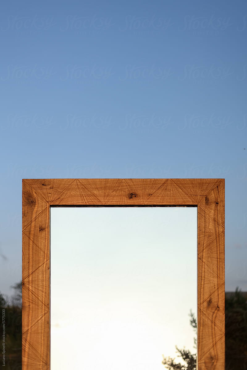 Handmade wood mirror frame reflecting blue sky and tree outdoors