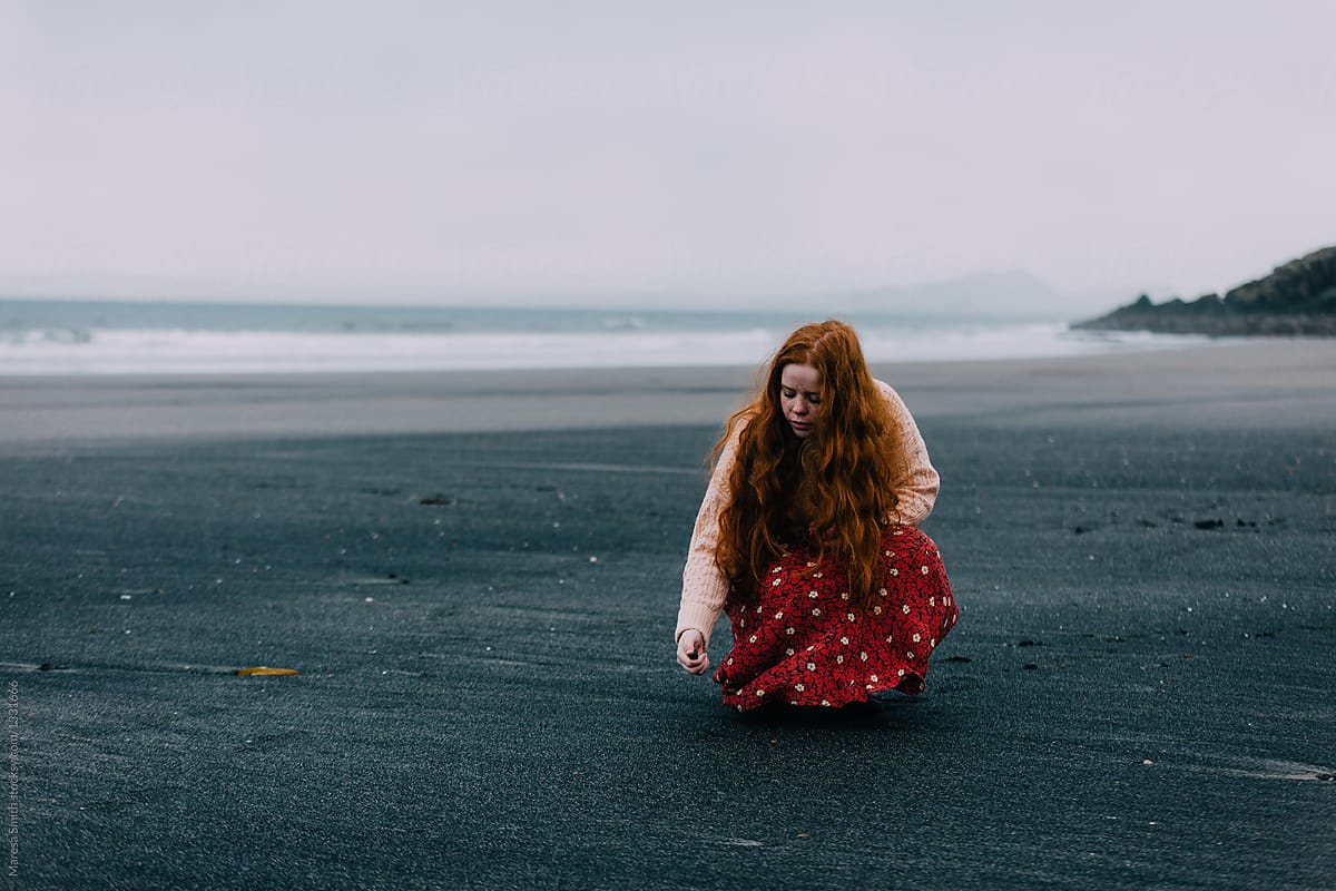 A beach comber collects sea-glass on a beach with black sand in winter