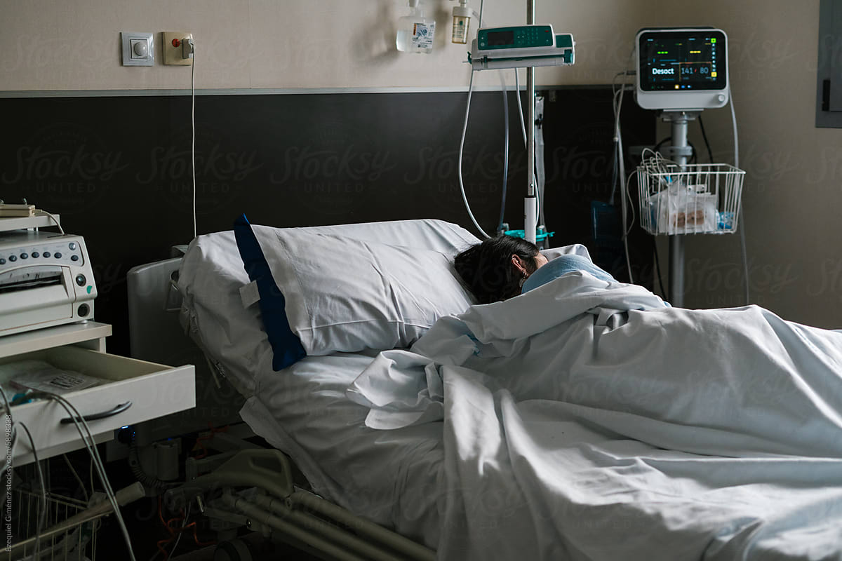 Patient in hospital bed in ward with medical equipment