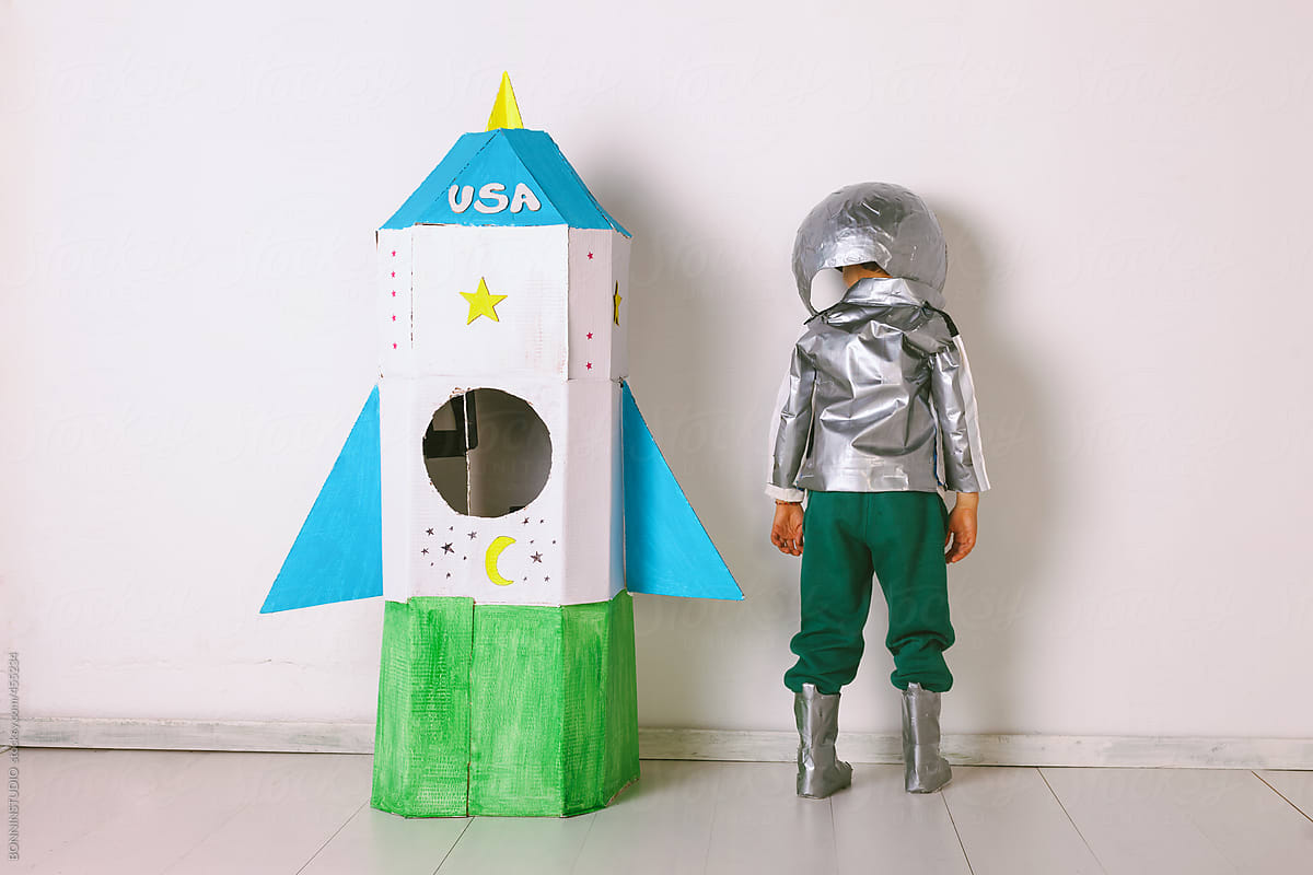 Back view of young boy wearing handmade astronaut uniform next to a diy rocket.