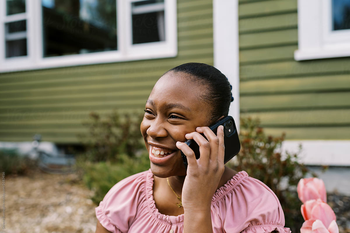 Smiling black girl talking on her smartphone while sitting in her yard