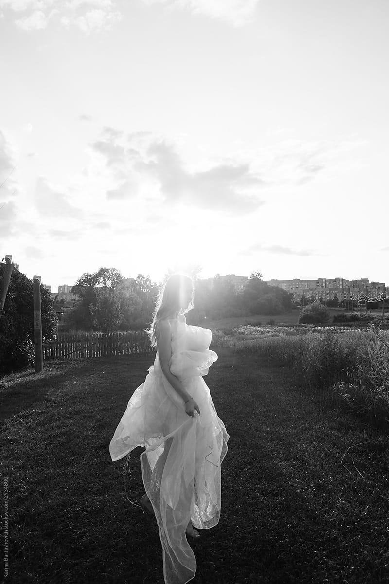 black and white photo of a girl in a white airy dress standing on a road in the countryside