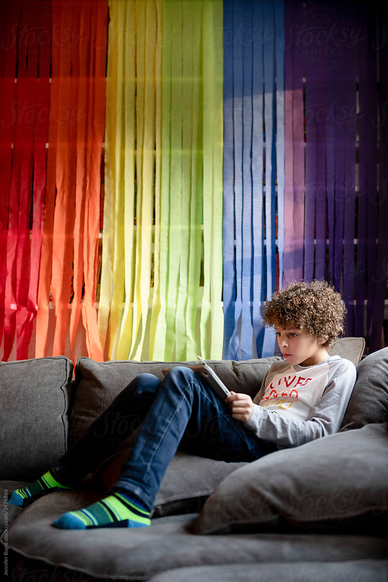 Boy Reads On Couch In Front Of Rainbow Streamers by Stocksy Contributor  Jennifer Bogle - Stocksy