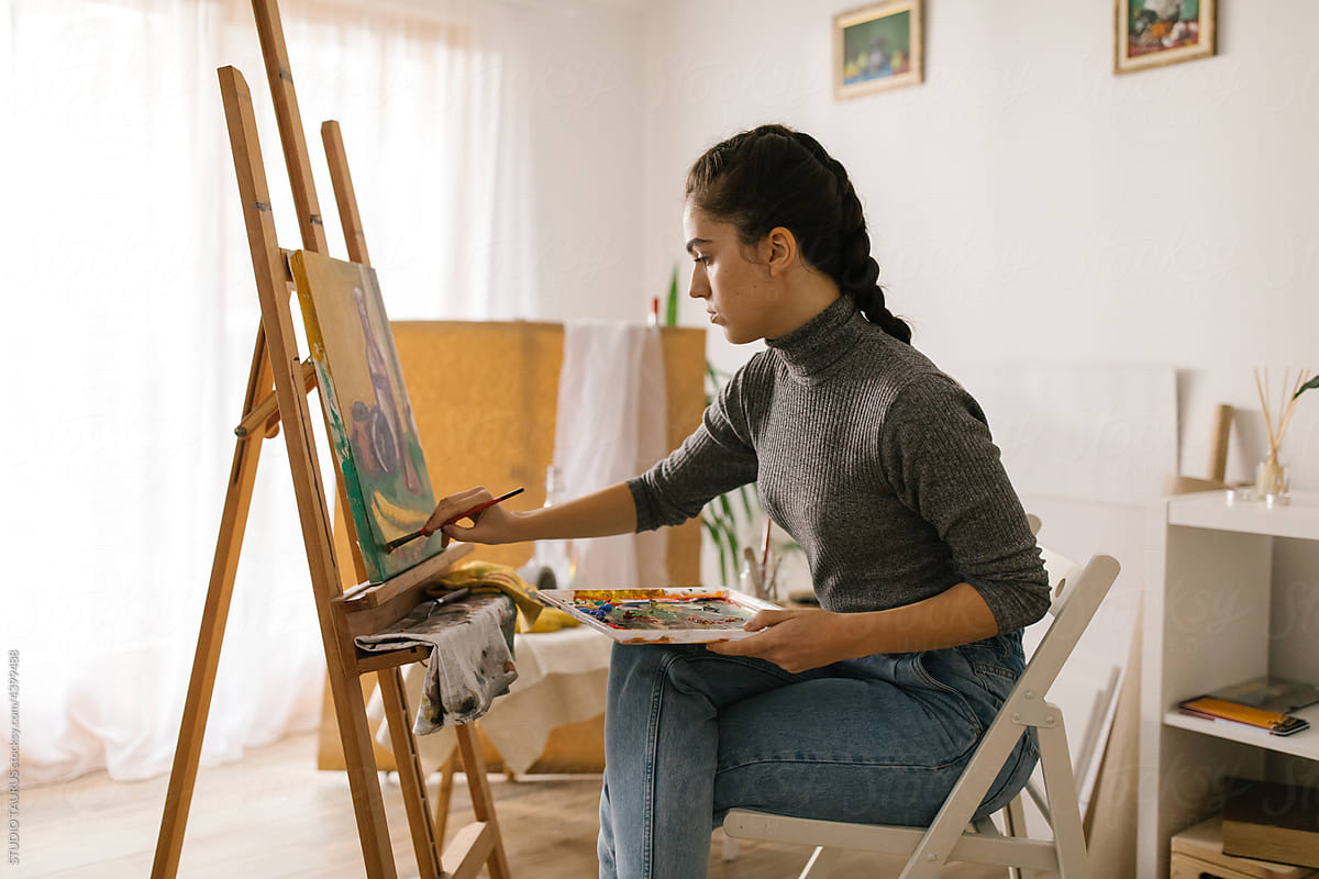 Painter sitting and painting on canvas in the studio