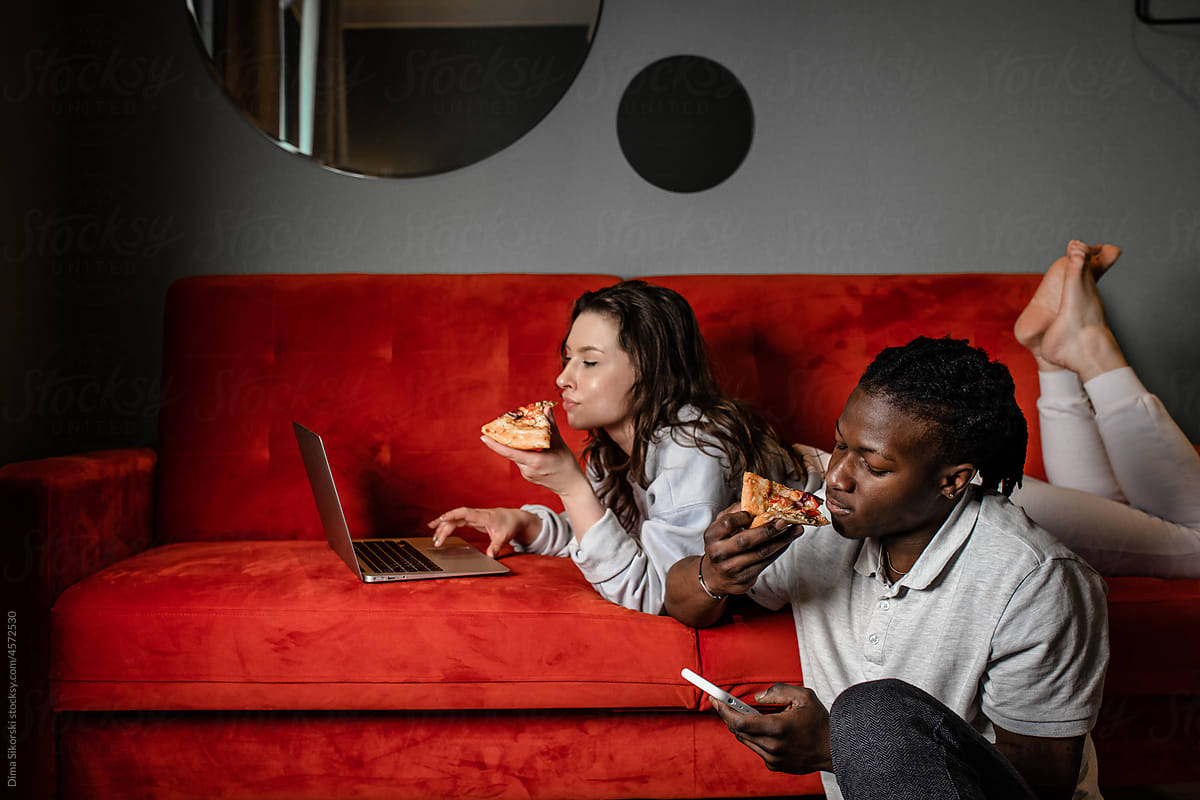 A married couple eats pizza and uses a laptop and a smartphone