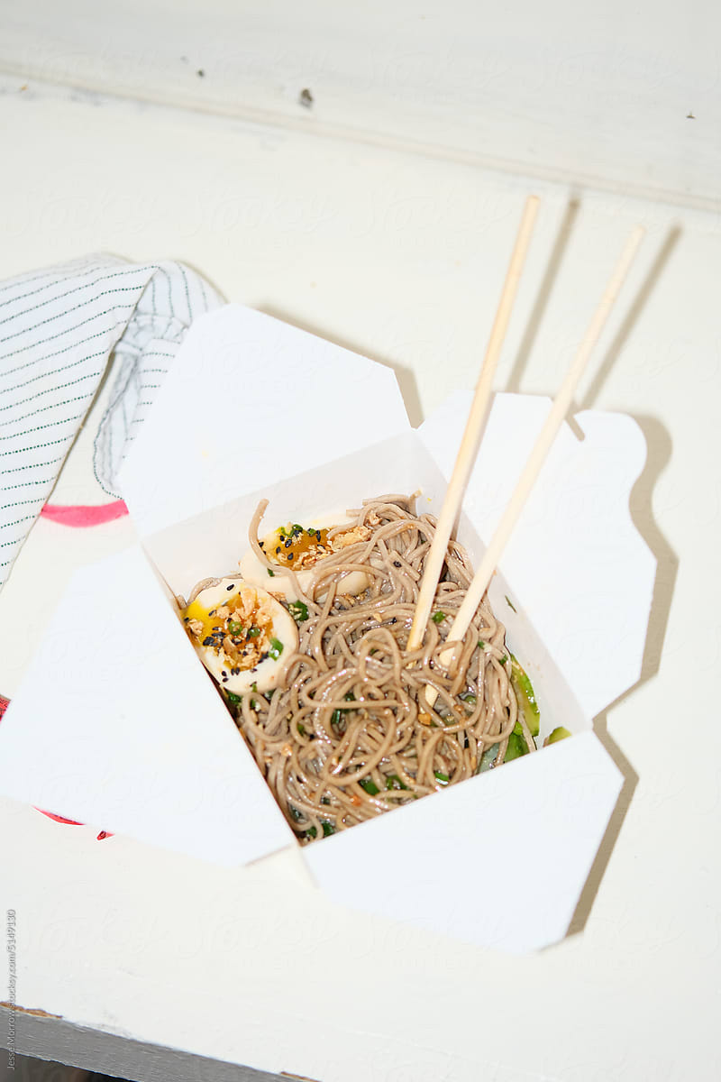 Carton of to-go food noodles and chop sticks on counter top.