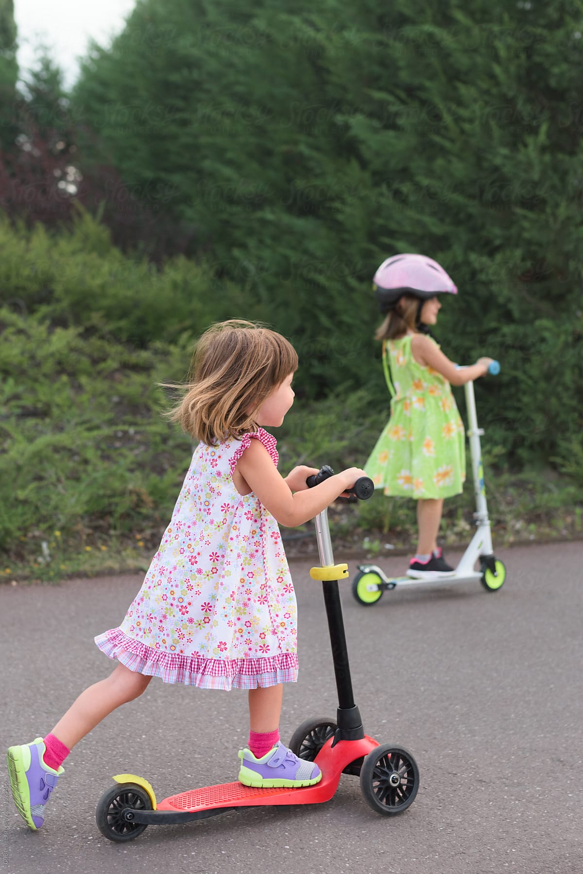 Two little girls rolling with toy scooters outdoor
