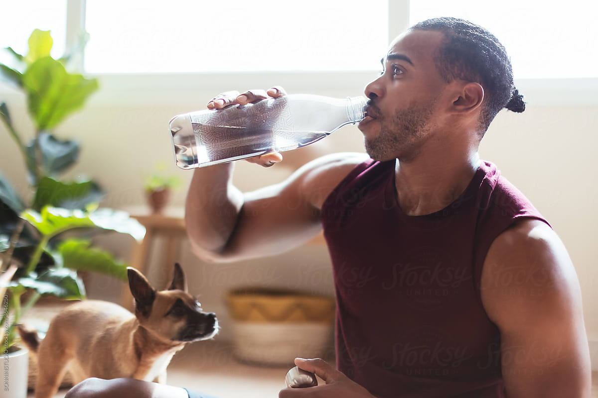 African American dog owner drinking water after workout