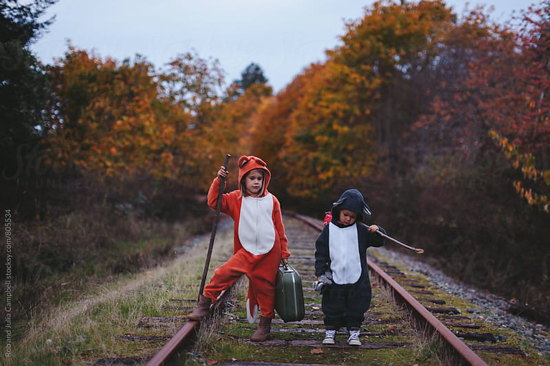 Kids dressed up like fox and raccoon walking on train tracks