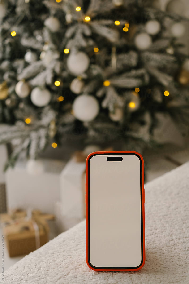 Smartphone with blank screen over sofa in room with Christmas tree