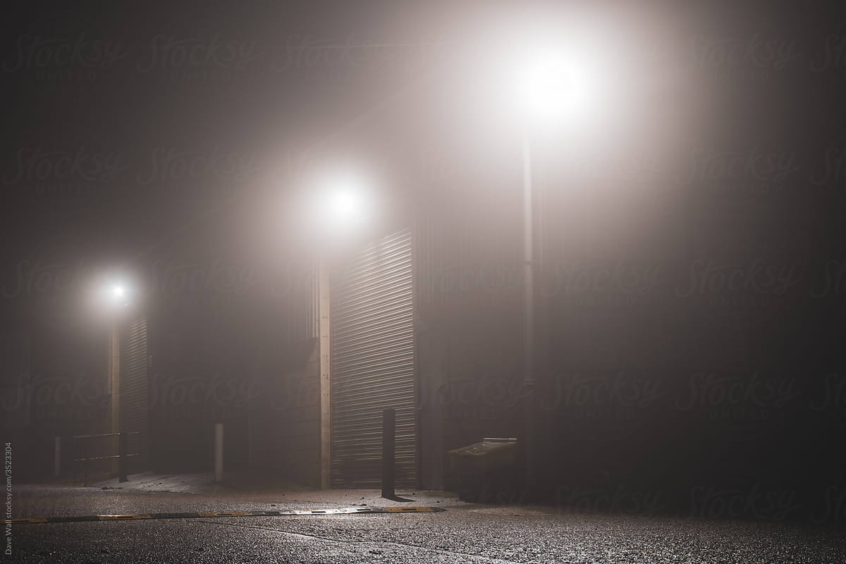 The doors of a warehouse lit up by security lights on a foggy night