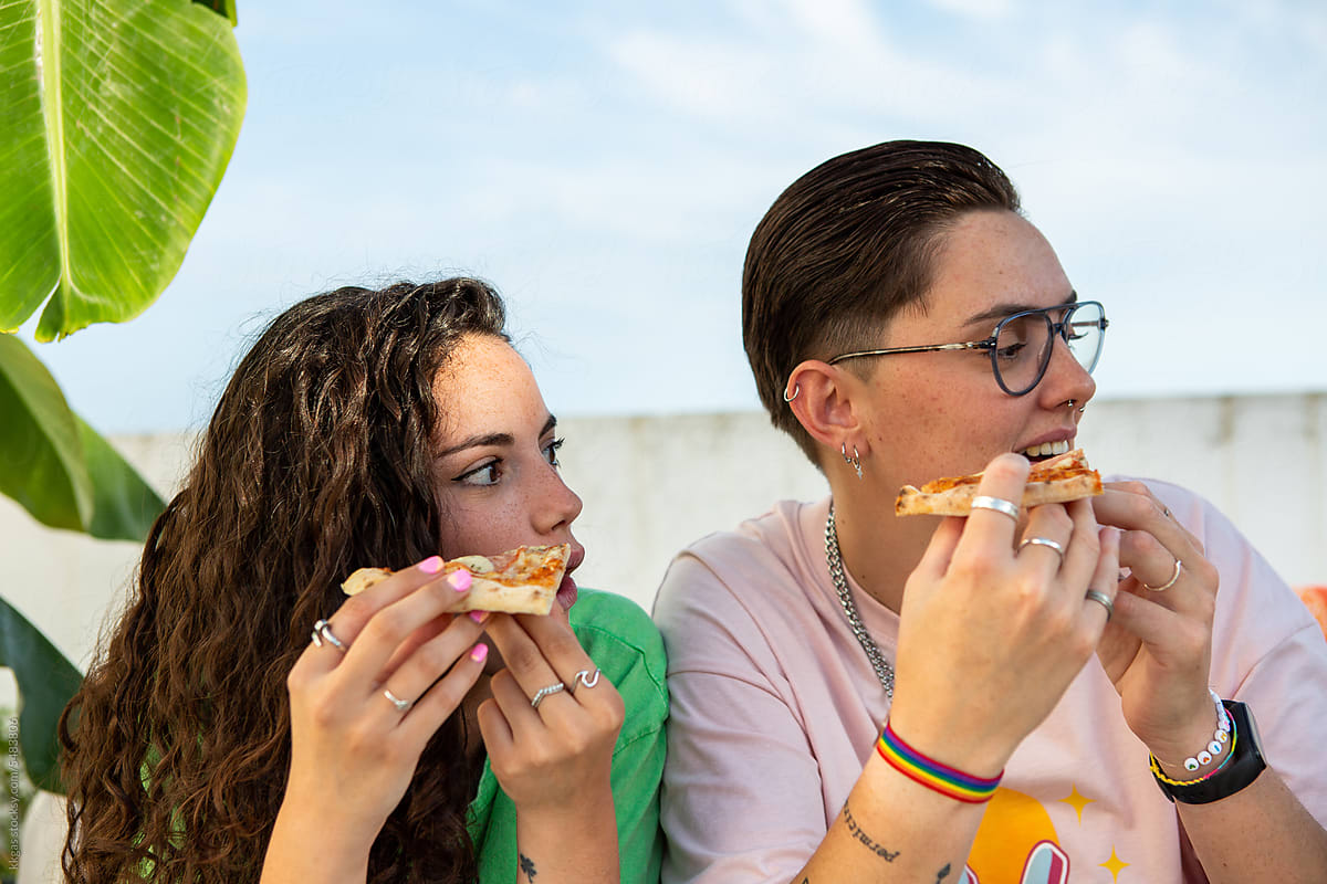 Two people holding pizza look to the side