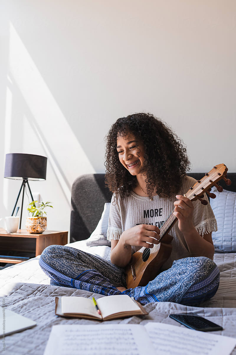 Cheerful Woman playing Ukelele On Her Bed