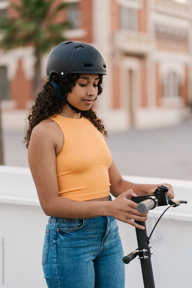 Black woman in helmet starting electric scooter in city