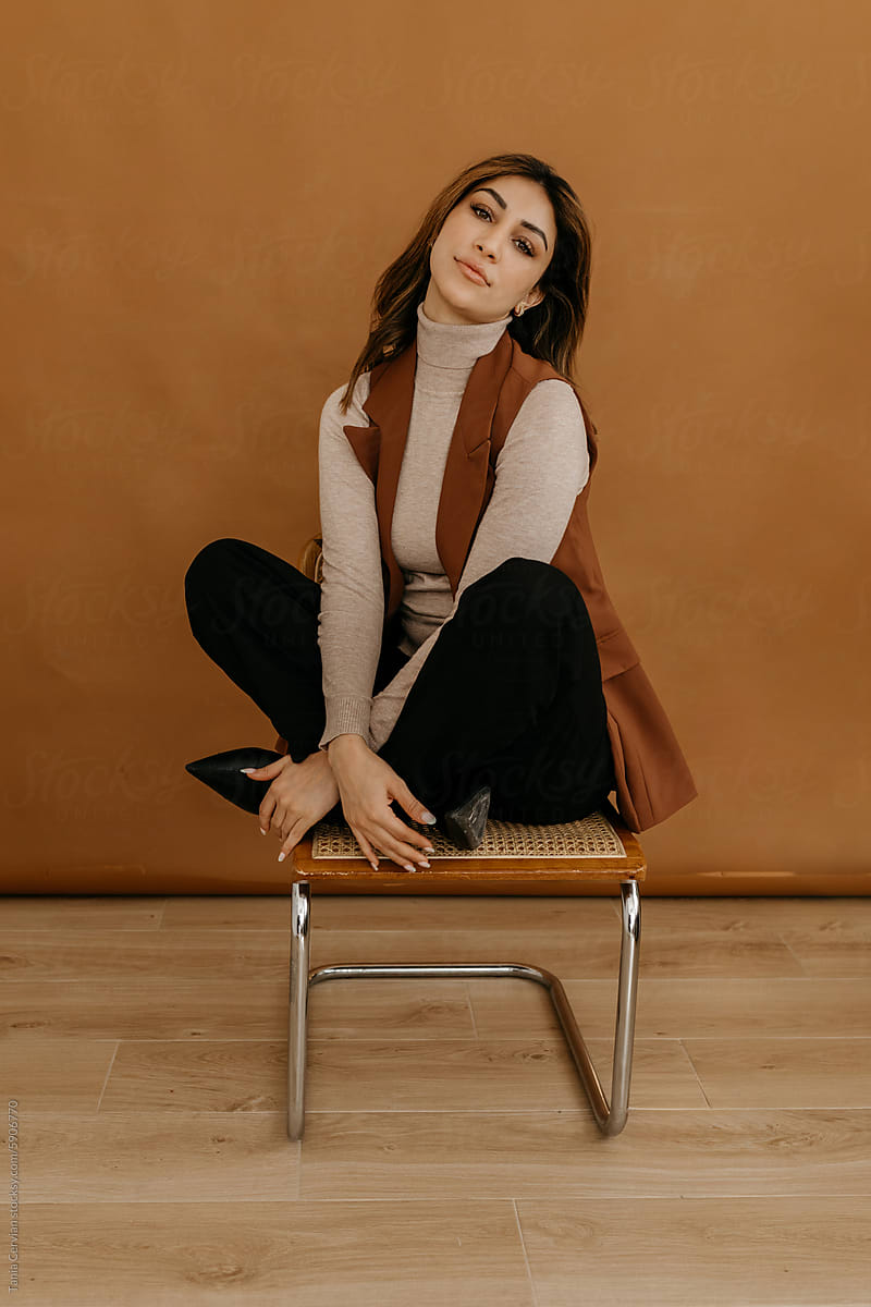 Positive stylish young woman sitting on chair in studio
