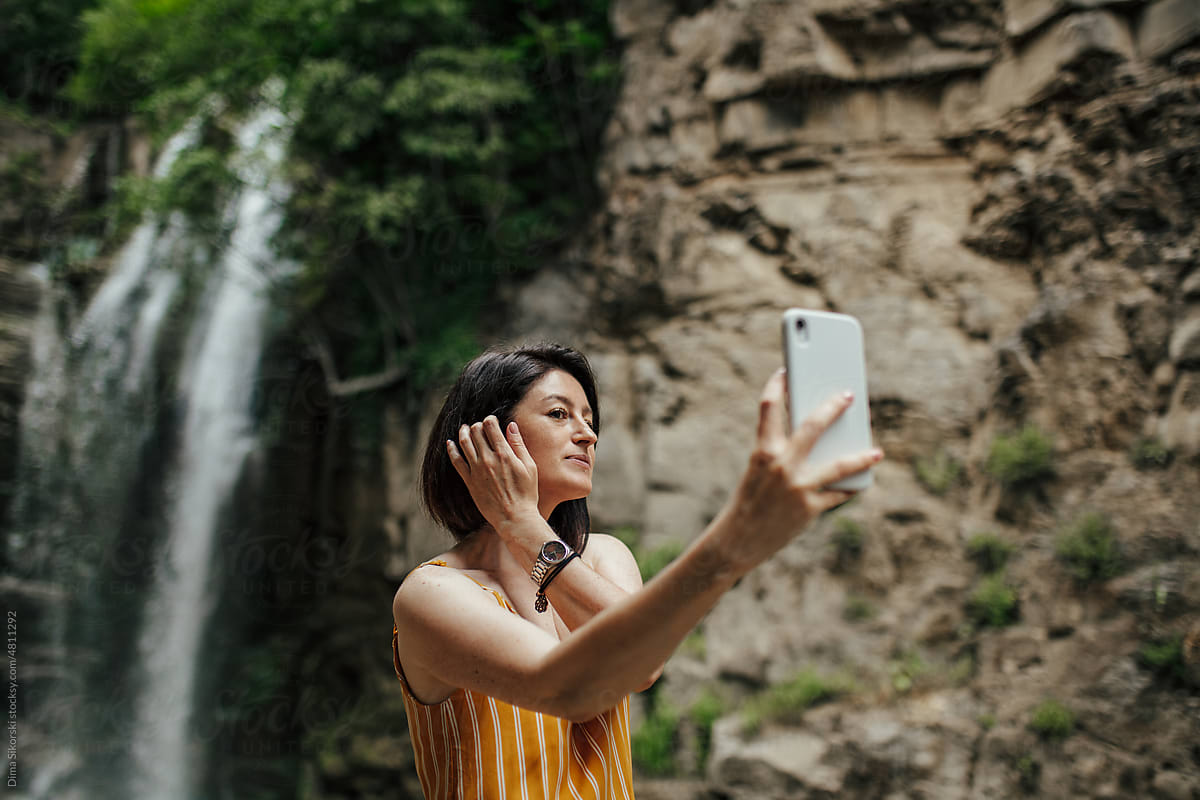 Attractive girl takes a selfie near a beautiful waterfall
