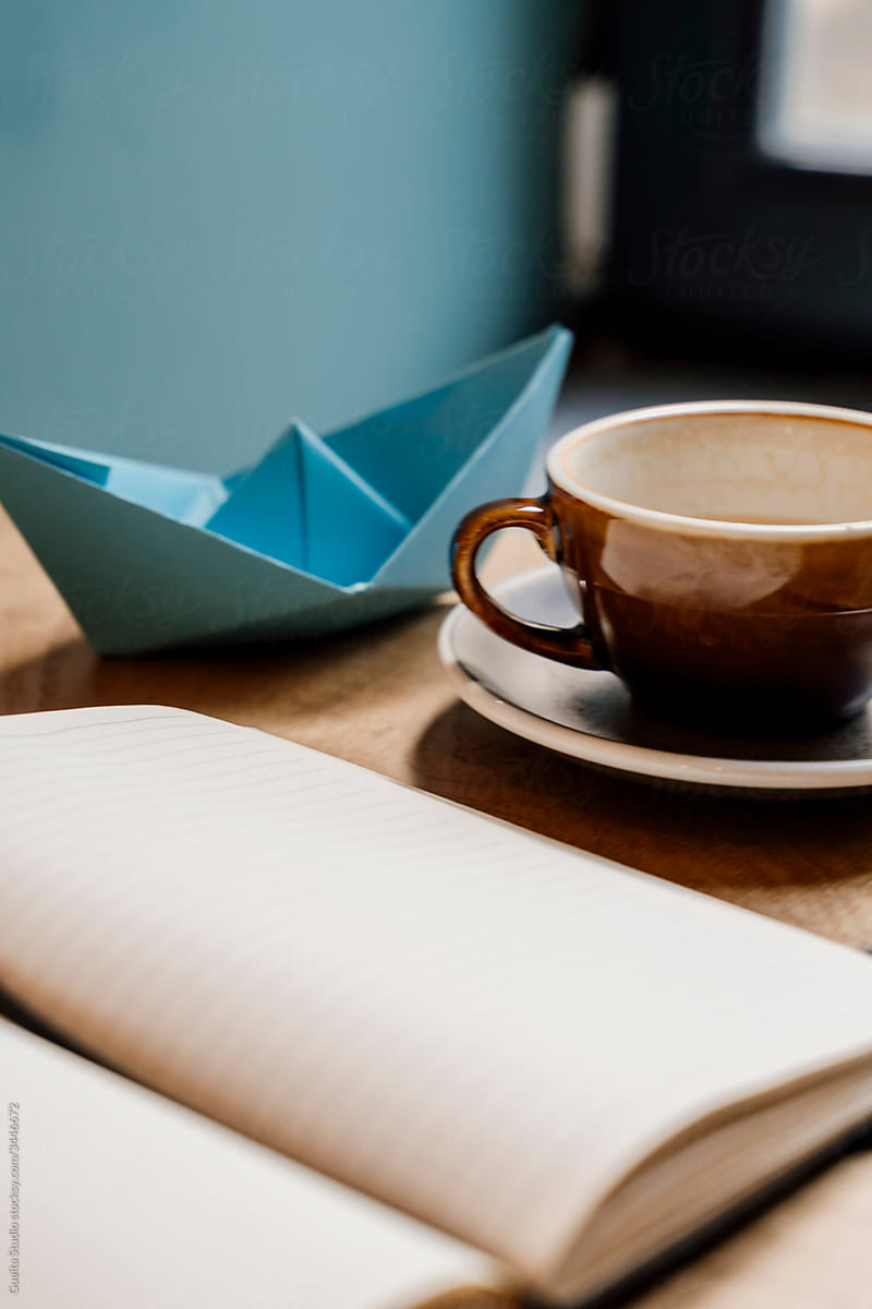 Closeup of notebook coffe mug and origami boat on table